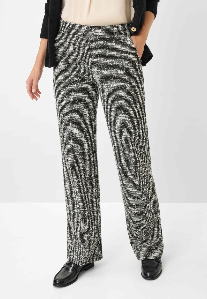 Pantalons en tissu tissé texturé noir et blanc, présentant un design à jambe droite et des poches latérales, associés à des chaussures noires.