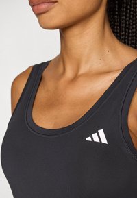 Svart atletisk tanktopp med rund halslinning, glatt tekstur og hvit logo på venstre side. Elastisk stoff for komfort.