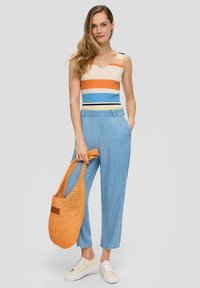 Gestreiftes, geripptes Oberteil in Orange, Weiß und Blau; hellblaue Hose; gestrickte orangefarbene Tasche; beigen Sneakers mit weißen Sohlen.