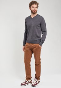 Pull V en gris foncé, pantalon slim en marron, et baskets bordeaux avec des accents blancs ; tenue décontractée avec une finition en tricot texturé.