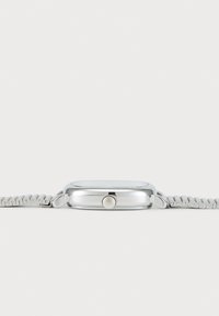 Montre en métal argenté avec un boîtier rectangulaire, couronne texturée sur le côté et bracelet en métal à maillons, le tout sur un fond blanc.