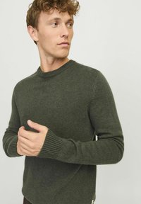 Suéter de punto verde oscuro con cuello redondo, puños acanalados y un acabado texturizado, que presenta mangas ajustadas y una forma de cuerpo relajada.