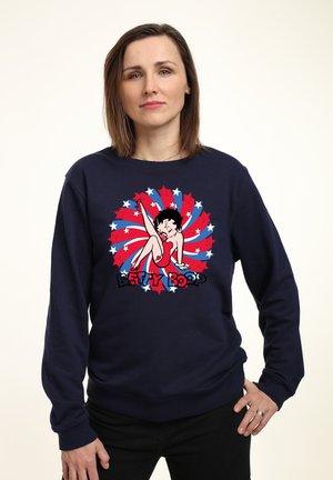 Mørkeblå sweatshirt med lange ærmer, der har et grafisk print af Betty Boop på en rød og blå stjernemotiv baggrund. Blødt stof, afslappet pasform.