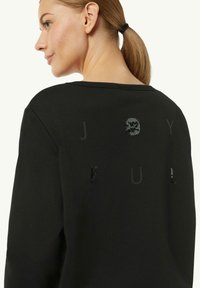 Czarny sweatshirt z okrągłym dekoltem i luźnym krojem. Ozdobiony teksturowanymi literami oraz designem czaszki z cekinami na plecach.