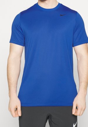 Un mannequin porte un T-shirt Nike bleu uni à manches courtes, avec un petit logo noir sur la poitrine, ainsi qu’un pantalon noir.