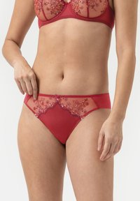 Culotte en dentelle rouge transparente avec des broderies florales, présentant un dos lisse et des accents décoratifs à la taille.