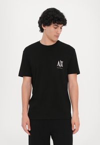 Svart bomulls t-skjorte med korte ermer, rund hals og liten hvit logo på venstre bryst. Glatt tekstur, enkelt design.