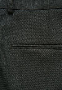 Schwarzer, strukturierter Stoff mit einem dezenten Webmuster, der über eine schmale horizontale Paspeltasche und gestickte Details zur Verstärkung verfügt.