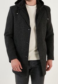 Abrigo oscuro con textura y capucha, con cierre frontal de botones y tela interior de contraste. Diseño sencillo, adecuado para uso casual.