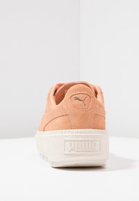 Meruňková semišová teniska s tlustou bílou gumovou podrážkou, se zdvihnutým logem PUMA na zadní straně a švy podél stran.