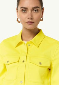 Bright yellow denim jacket with a pointed collar, two chest pockets, gold-tone hardware, and visible stitching details.