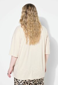 Beige ylipitkä t-paita lyhyillä hihoilla, rento istuvuus, pehmeä rakenne ja kaareva helma, yhdistetty kuvioituun leopardikuosisukkahameeseen.