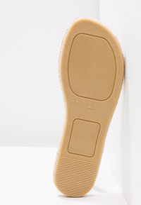 Semelle de chaussure en caoutchouc avec une surface beige lisse, des zones texturées et un emblème surélevé portant les inscriptions "37" et "FABRIQUÉ EN ESPAGNE."
