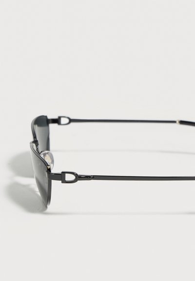 Λεπτά μαύρα ορθογώνια γυαλιά ηλίου με μεταλλικό σκελετό, εμφανιζόμενα από το πλάι σε λευκό φόντο.