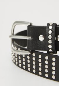 Ceinture en cuir noir avec une boucle en métal argenté et des clous circulaires uniformément espacés le long de la sangle pour un détail et une texture supplémentaires.