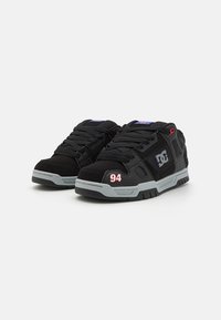 Sapatos de skate pretos com uma língua almofadada, sola cinza, detalhes em vermelho e o número "94" em vermelho na lateral. Design com atacadores, material durável.