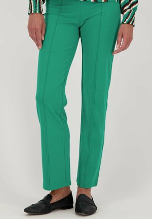 Pantalons stretch verts avec une taille plate et des coutures verticales. Associés à des chaussures noires à enfiler. Texture lisse et coupe ajustée.