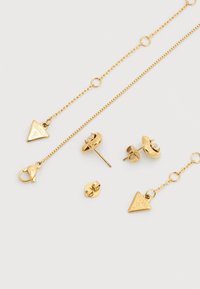 Σετ χρυσών κοσμημάτων με τρίγωνο μενταγιόν, υφασμένη αλυσίδα, σκουλαρίκια με καρφί και διαφανή πέτρα, καθώς και κούμπωμα αστακού. Κομψό και λαμπερό φινίρισμα.