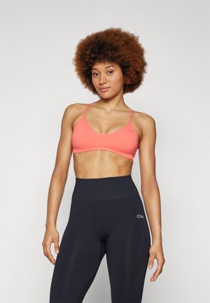 Koral sports BH med tynne stropper og glatt tekstur, kombinert med høyhåndte svarte leggings med en logo. Begge plaggene sitter tett.