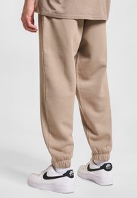 Beżowe dresy o luźnym kroju, ze ściągaczami w kostkach i szwami bocznymi, zestawione z białymi sneakerami Nike z czarnym logo.