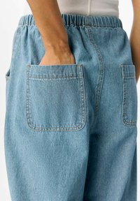 Pantaloni in denim azzurro chiaro con vita elastica, dotati di due tasche laterali e dettagli di cucitura in vista.