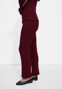 Burgundowa dzianinowa bluzka z prążkowanym wzorem i spodnie z rozszerzonym dołem, w połączeniu z czarnymi balerinami z srebrnymi ćwiekami. Gładka faktura, dopasowany fason.