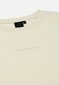 Crème katoenen T-shirt met een ronde halslijn, voorzien van reliëf 'TOMORROWLAND' tekst aan de voorkant en een zwart label aan de achterkant voor maatindicatie.