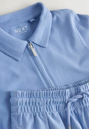 Gai zils polo krekls ar priekšējo rāvējslēdzēju, teksturētu apkakli un saskaņotas šortus ar auklu un elastīgu jostu, kas izgatavoti no gludas auduma.