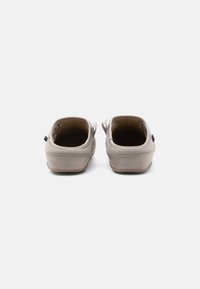 Beige slip-on sko med en tekstureret stofoverdel, gummisål og kontrasterende sort detalje ved hælen. Rund ryg for nem påtagning.