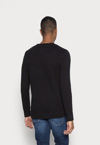 Svart stickad tröja med långa ärmar, rund halsringning och ribbade muddar och fåll, i kombination med blå denimjeans. Utsikt från baksidan.