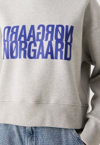 Grå hettegenser med et blått opp-ned grafisk tekst "Nørgaard" på forsiden. Mykt stoff med en avslappet passform og ribbede mansjetter.