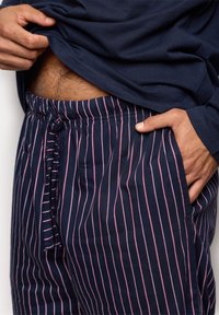 Marineblå stribede pyjamasbukser med hvide og lyserøde lodrette striber, elastisk talje med snoretræk og sidelommer. Blød stoftekstur.