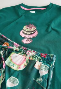 Zielony sweter z grafiką ciasta oraz kwiatowe szorty piżamowe z kolorowymi wzorami. Elastyczny pas i regulowany sznurek.