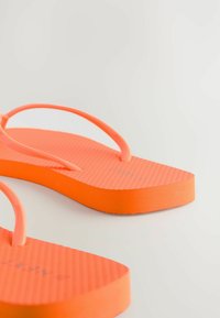 Oranžid plätud tekstureeritud tallaga ja õhukeste rihmadega. Jalaosa on tasase kujundusega, luues lihtsa ja kerge jalatsivaliku.