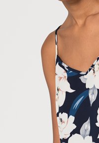 Canotta a fantasia floreale in blu navy, con spalline sottili, scollatura a V e un tessuto leggero impreziosito da fiori rosa e bianchi.