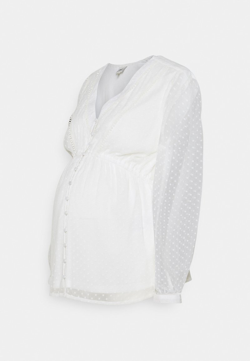 Blusa da maternità bianca con pois testurizzati, chiusura a bottoni, scollatura a V e vita arricciata. Presenta maniche lunghe e trasparenti e un tessuto morbido.