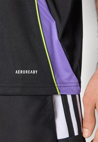 Svart atletisk skjorte med lilla og grønne sideakenter, med 'AEROREADY' logo, laget av fukttransporterende materiale.