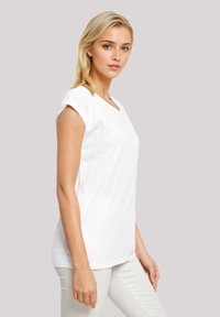 White cotton t-shirt with short sleeves, v-neck design, relaxed fit, featuring a smooth texture and minimal detailing, worn with light-colored pants.