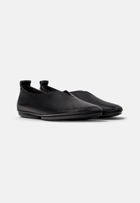Scarpe slip-on nere in pelle con una texture liscia, punta arrotondata, design minimale e inserti elastici sul tallone per una facile calzata.