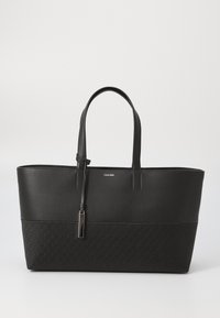 Černá taška přes rameno s hladkou horní částí a texturovaným dnem, které má jemný monogramový vzor. Úzké uši a dekorativní táhlo zipu.