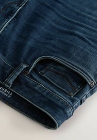 Dunkelblaue Jeans aus Denim mit glatter Textur, im klassischen Fünf-Taschen-Design, mit kontrastierenden Nähten und einem einfachen Knopfverschluss.