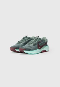Nike bėgimo bateliai su kvėpuojančia tinklelio viršutine dalimi žalia spalva, akcentuoti bordo pirštu ir mėtų žalio padu. Yra rožinės detalės ir tekstūruoti raštai.