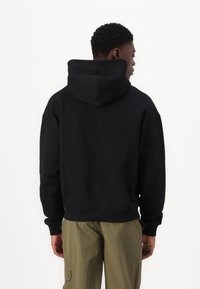 Felpa nera con cappuccio realizzata in tessuto morbido, dal fit rilassato e con polsini a coste, abbinata a pantaloni cargo verde chiaro.