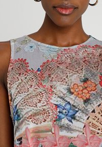 Ärmelloses Kleid mit einem bunten Blumenmuster, aus strukturiertem Stoff und filigranen, spitzenähnlichen Details in verschiedenen Rosa- und Blautönen.