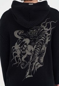 Felpa nera a costine con un design grafico di un teschio e una tigre, con linee e texture intricate, creando un dettaglio visivo notevole.