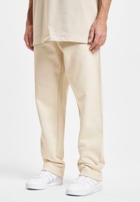 Beige bukser med brede ben lavet af en bomuldsblanding; har en glat tekstur, minimalistisk design og en let glans. Sammen med hvide sneakers.