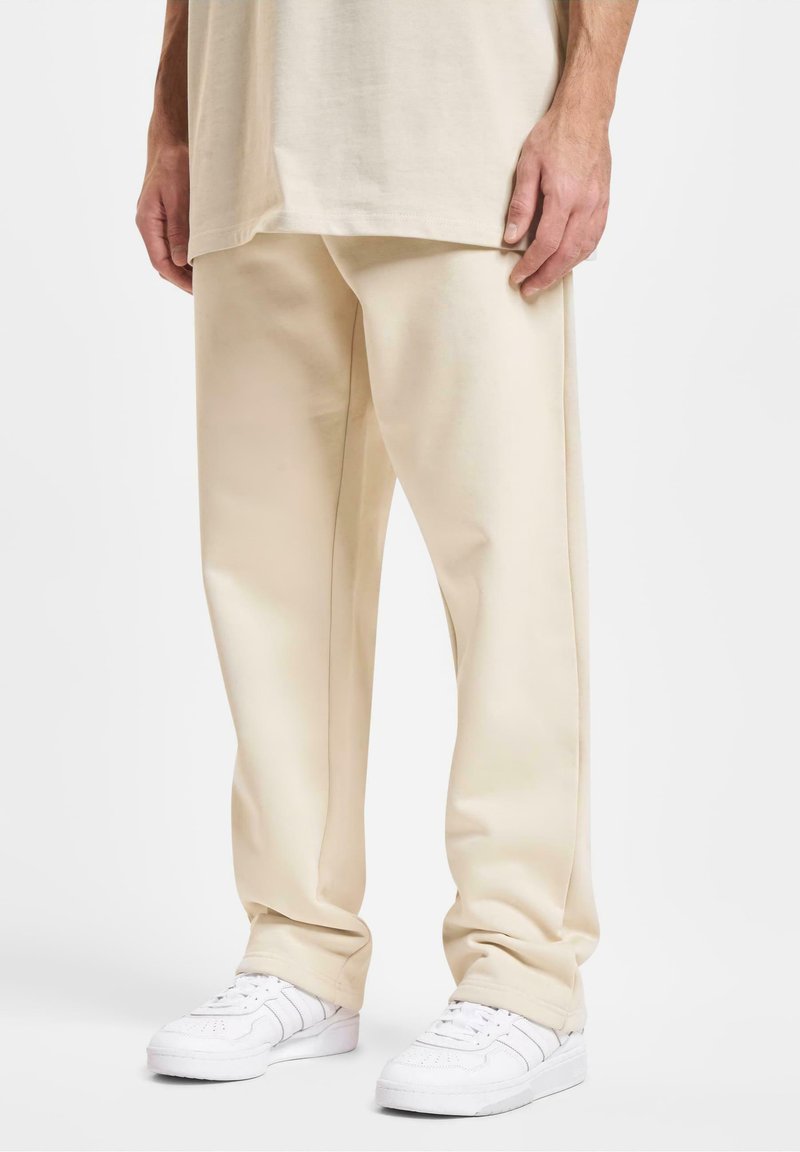 Beige bukser med brede ben lavet af en bomuldsblanding; har en glat tekstur, minimalistisk design og en let glans. Sammen med hvide sneakers.