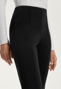 Leggings noirs taille haute en tissu extensible, avec des coutures verticales et une texture lisse. Gros plan sur le tissu et la coupe.