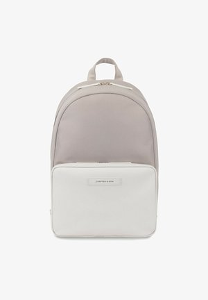 Mochila de tela gris con un compartimento inferior blanco, forma redondeada, asa superior y cremalleras doradas. Presenta una etiqueta de marca en la parte frontal.