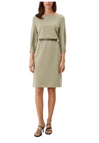 Sukienka w jasnooliwkowym kolorze z rękawami o długości trzy czwarte, dekoltem w łódkę oraz dopasowanym czarnym paskiem. Gładka faktura i długość do kolan.